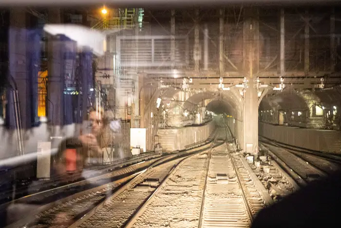 A view of the Hudson River Tunnel (which are dark and dusty), with reflection of people in a window